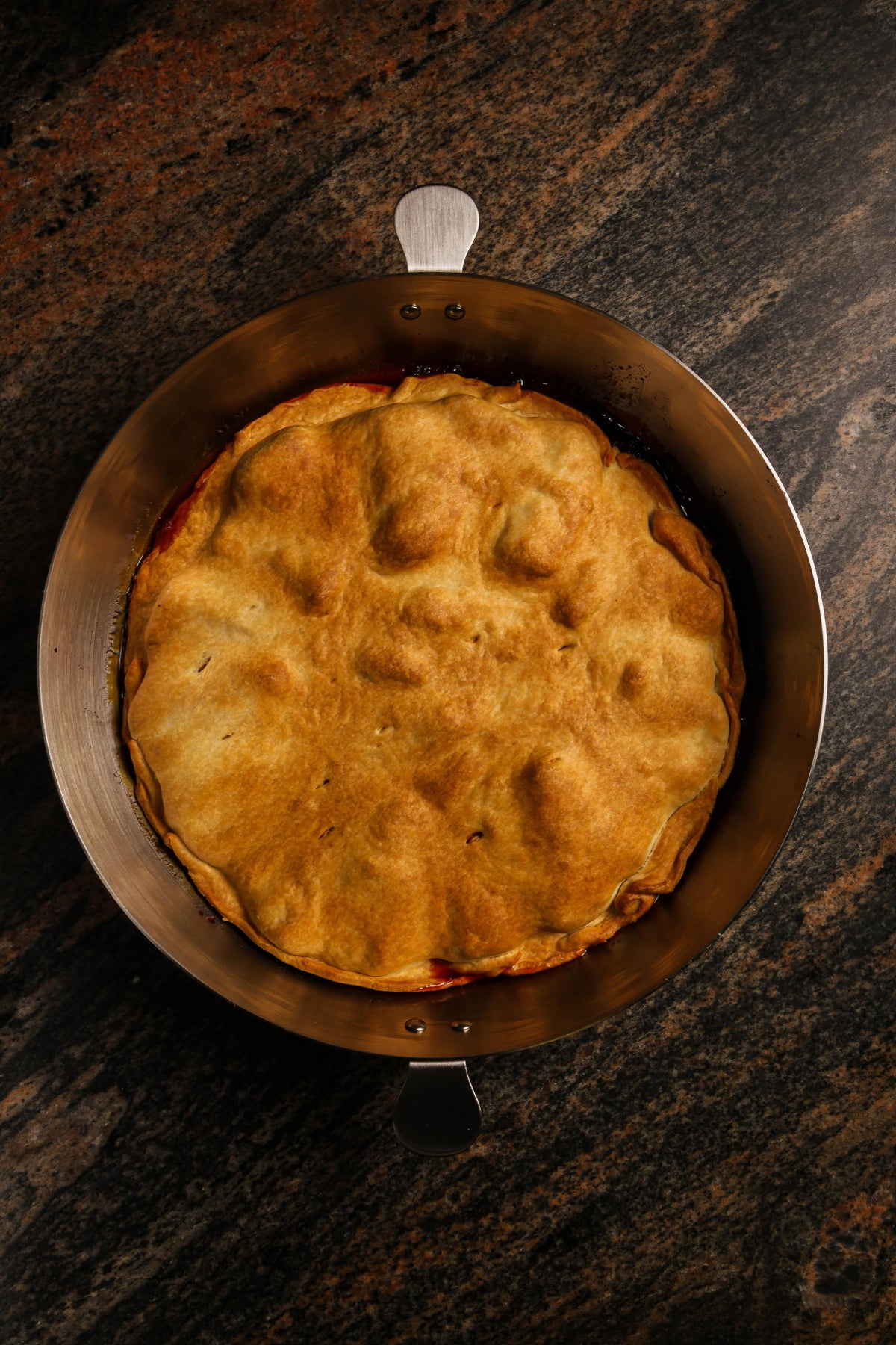 Freshly baked fruit pie with a golden brown crust in a round metal pan on a dark countertop.