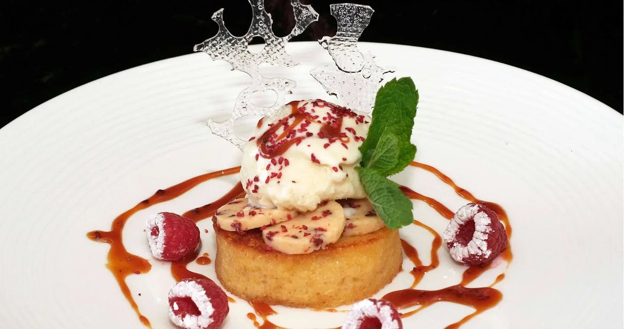 Artisan dessert with raspberries, mint, and caramel drizzle on a white plate