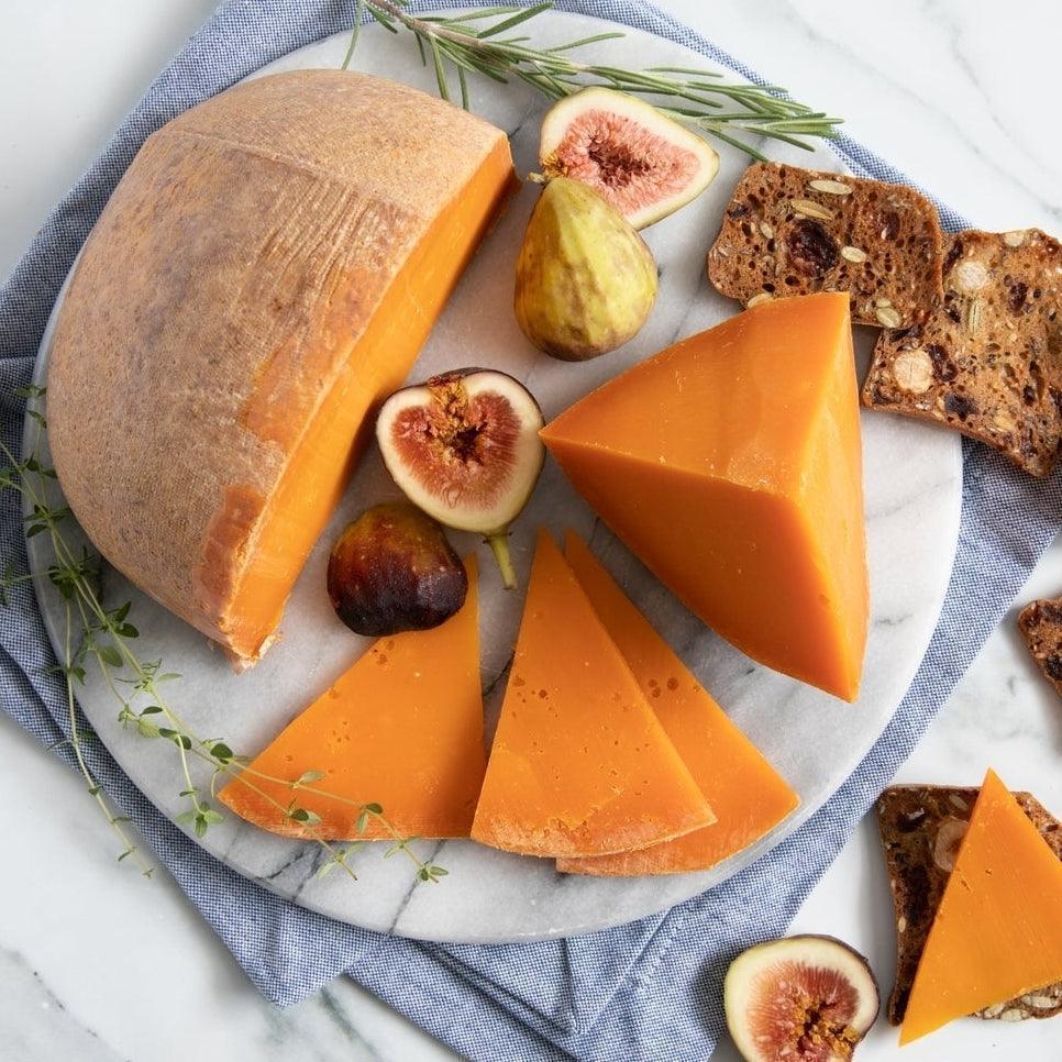 Artisan orange cheese wheel with figs, crackers, and herbs on marble board — premium, all-natural, gluten-free
