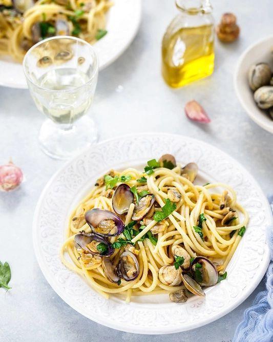 Pasta with clams, fresh herbs, and olive oil, served on a white plate with wine and garlic