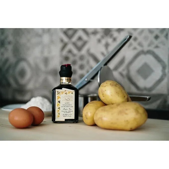Balsamic vinegar bottle with eggs, potatoes, and kitchen tools on a rustic countertop