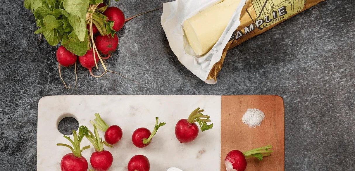 Fresh radishes on marble and wood cutting board with artisan French butter and sea salt