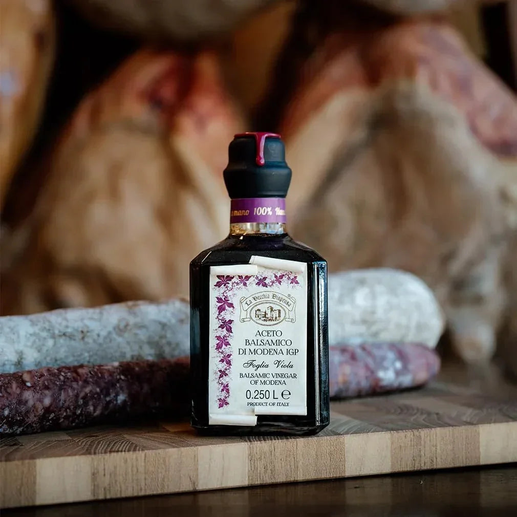 Balsamic vinegar of Modena IGP with purple fig leaf label, artisanal Italian condiment on wooden board with cured meats