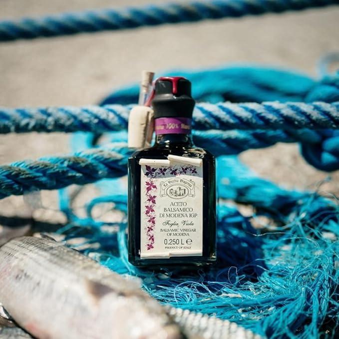 Balsamic vinegar of Modena IGP bottle on blue ropes with fish, artisan-made, premium quality