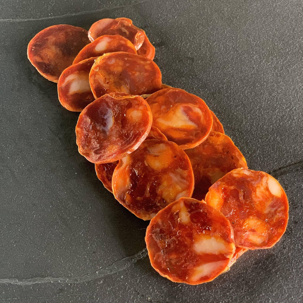 Sliced artisanal cured sausage on dark slate, premium quality, gluten-free, keto-friendly