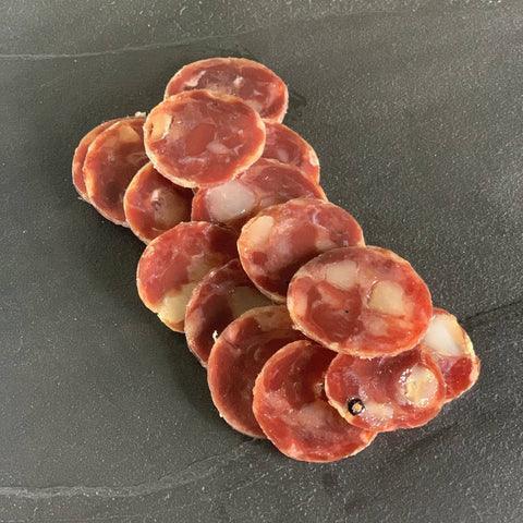 Cured duck salami slices fanned across dark slate, premium charcuterie