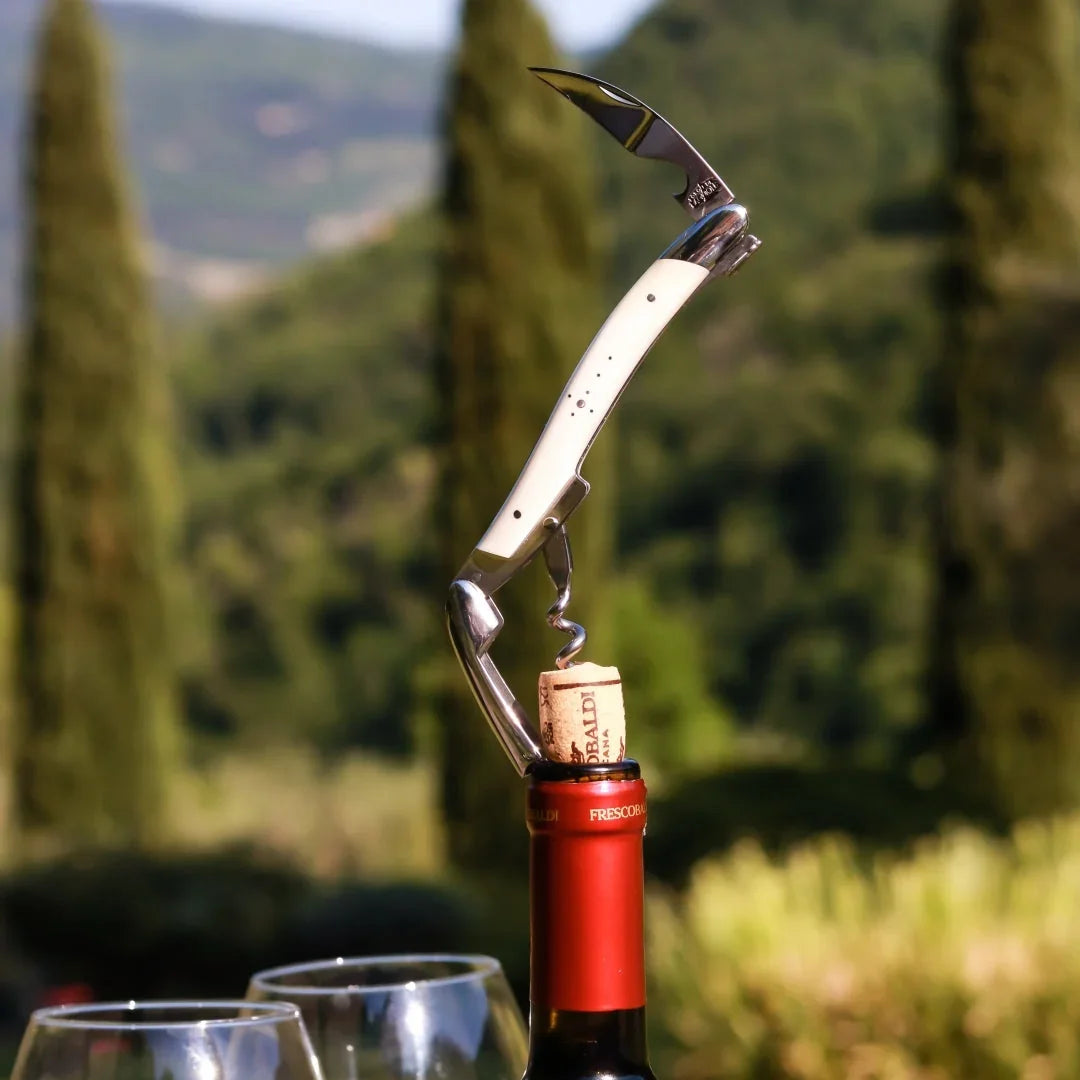 A white handled wine opener with a corkscrew and knife inserted into a wine bottle cap.