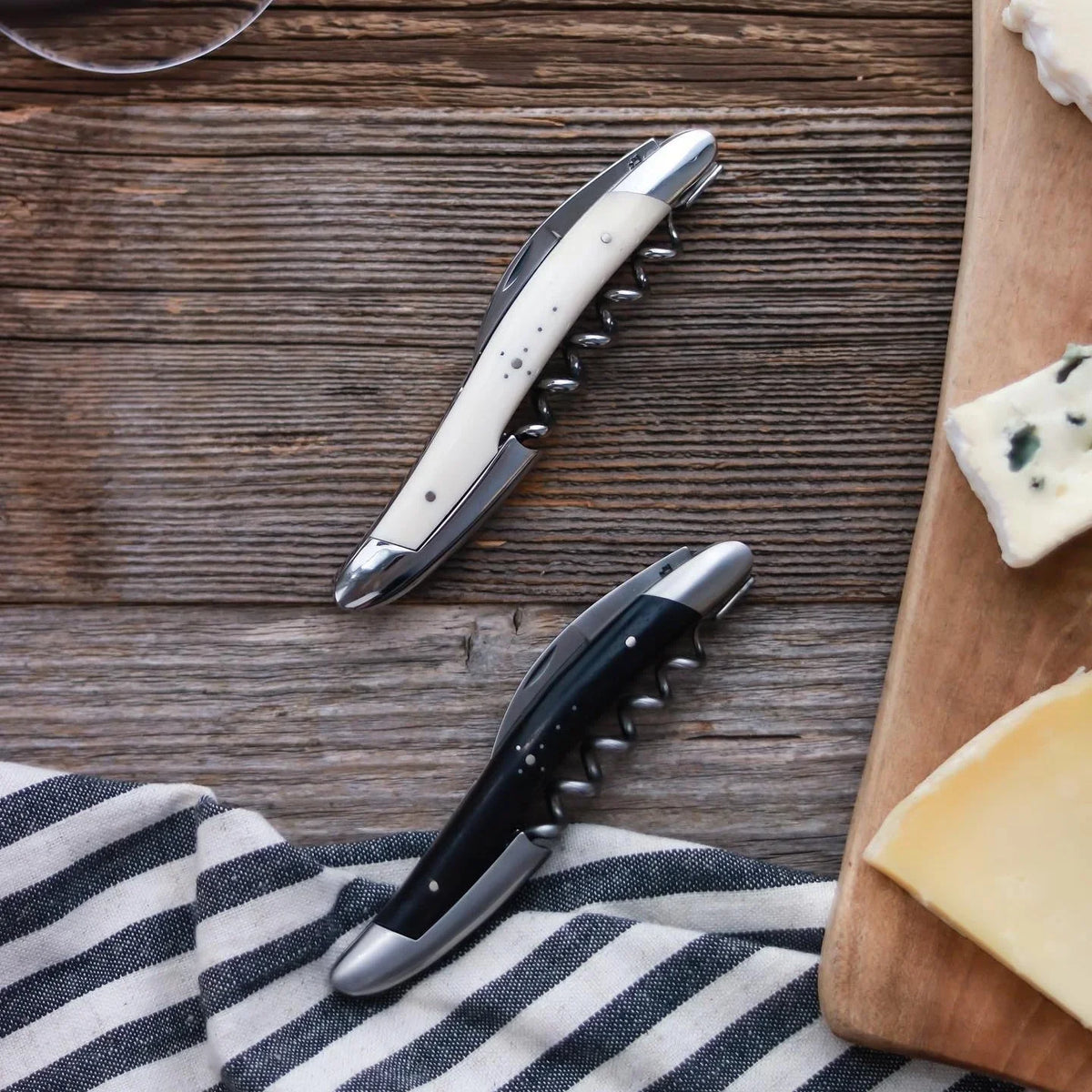 Two stainless steel cheese knives with white and black handles on a wooden surface.