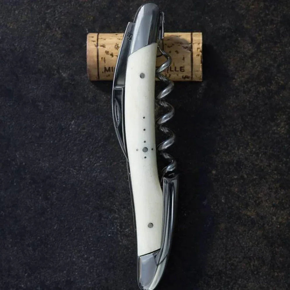 Elegant corkscrew with ivory handle beside wine cork on dark surface