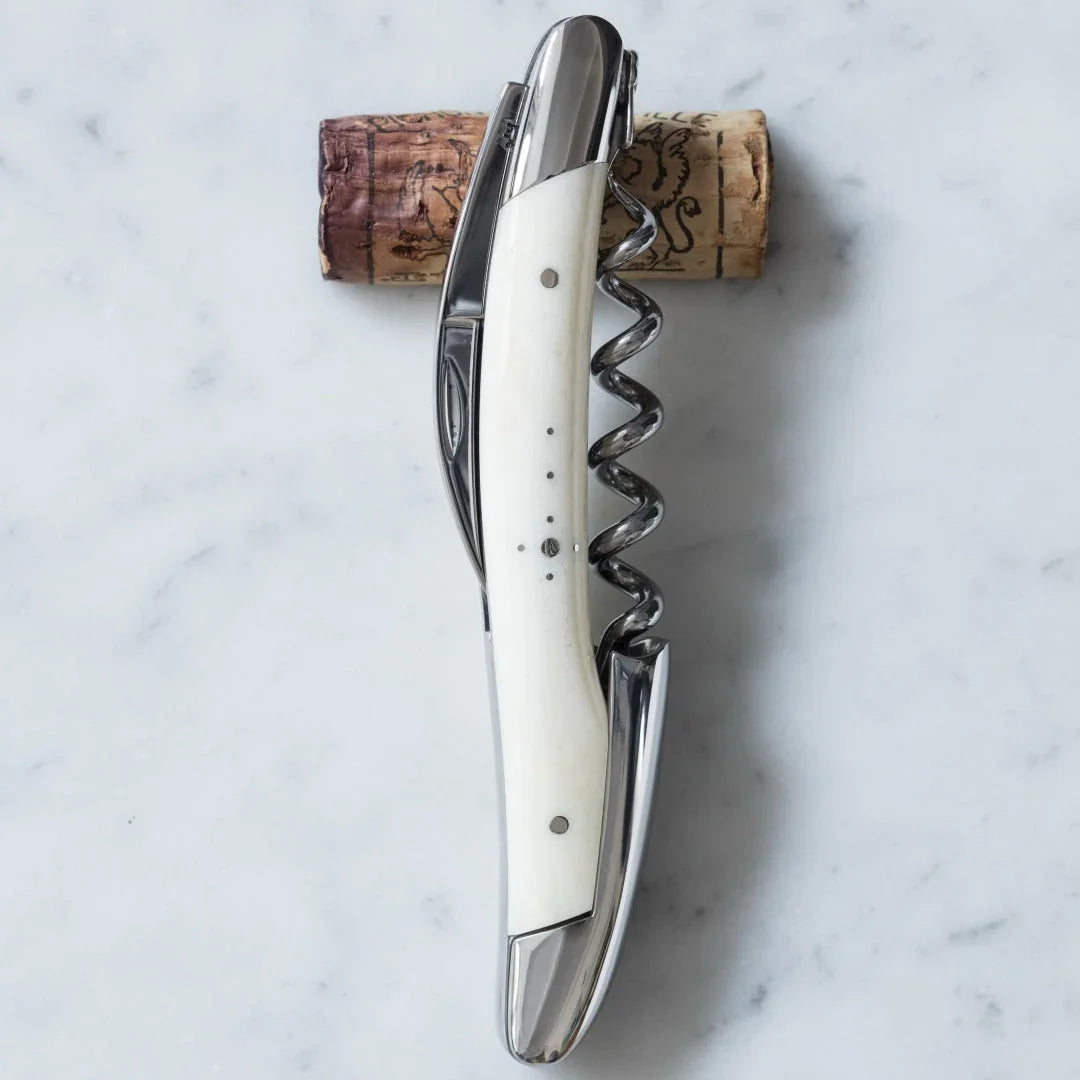 Silver waiter's corkscrew with a white handle resting on a wine cork over marble.