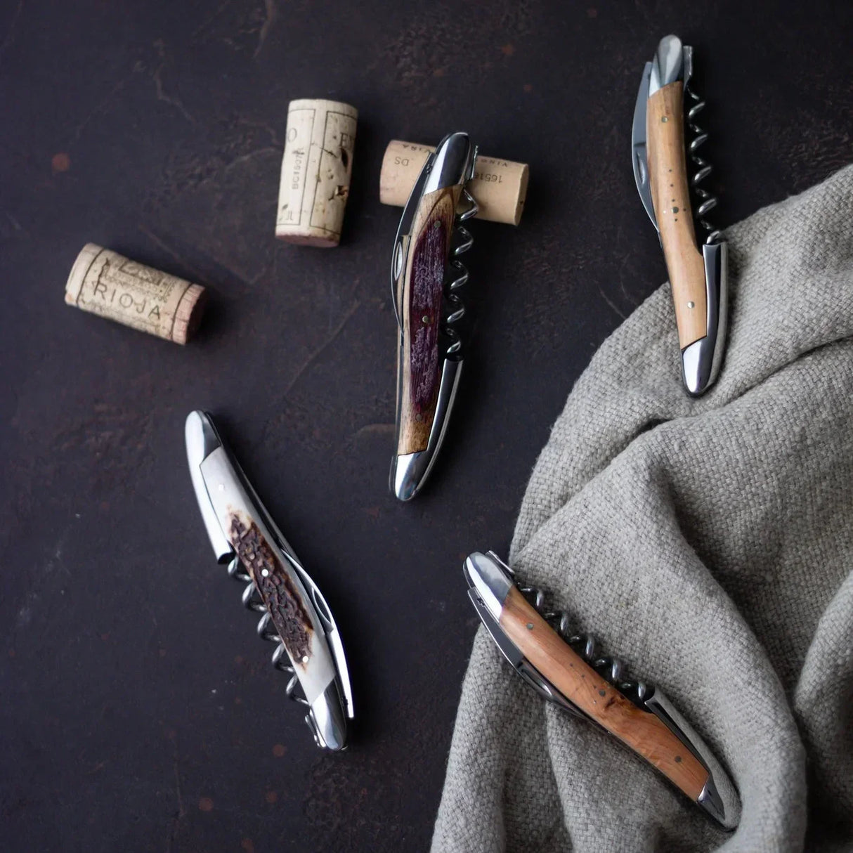 Elegant wine corkscrews with wooden and antler handles, styled with wine corks on dark surface