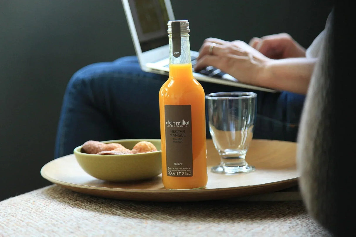 Alain Milliat mango nectar bottle with glass and snacks beside laptop, French premium beverage