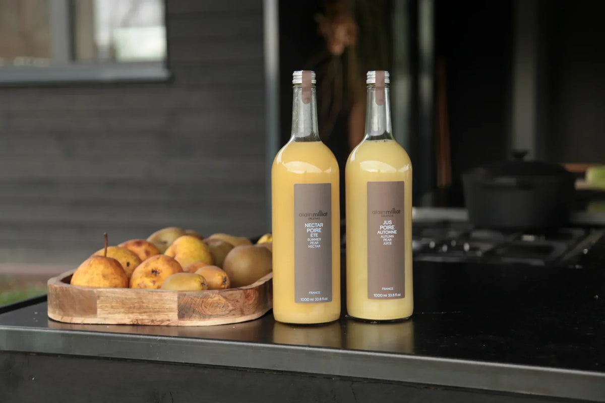 Two bottles of French pear nectar and juice beside fresh pears on a kitchen counter