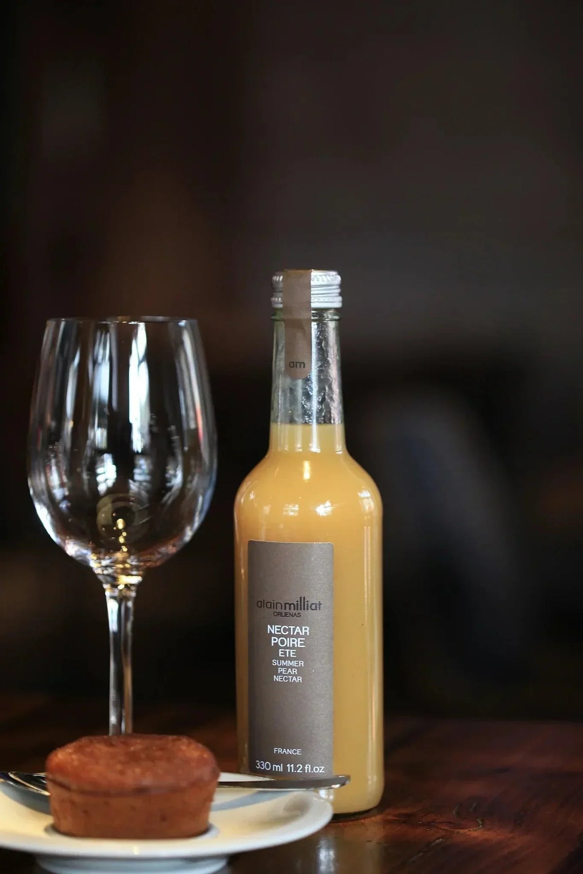 Alain Milliat Summer Pear Nectar bottle beside wine glass and small cake, French artisan beverage