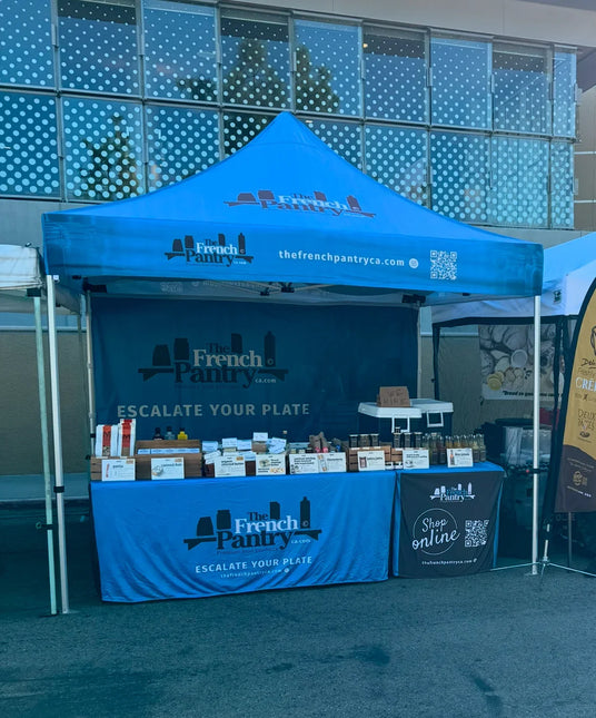 The French Pantry outdoor booth with premium French butter, cheese, jams, and artisan foods displayed under a blue tent.
