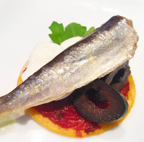 Sardine on a mini pizza base with tomato, black olive, and fresh herbs, Spanish tapa