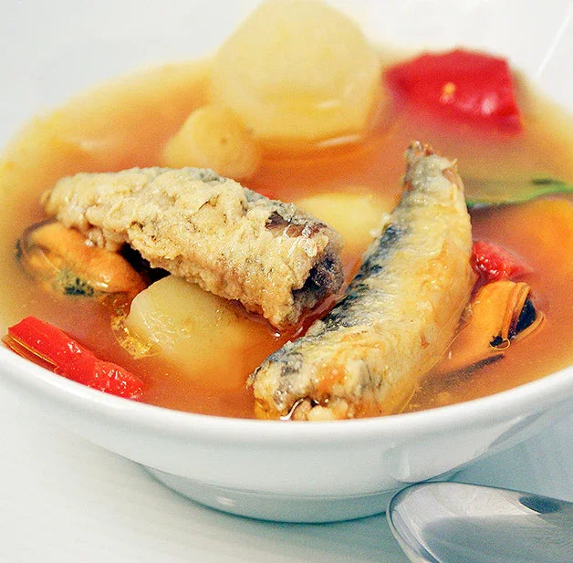 Bowl of sardine soup with vegetables and mussels in clear broth
