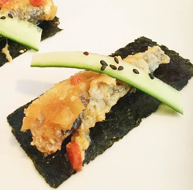 Sardine fillet with wakame seaweed, cucumber slice, and black sesame on a white plate