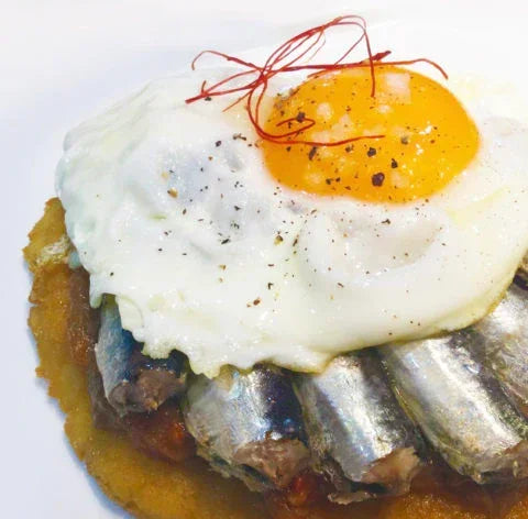 Sardines topped with sunny-side-up egg, black pepper, and saffron threads — artisan, clean-label, high-protein