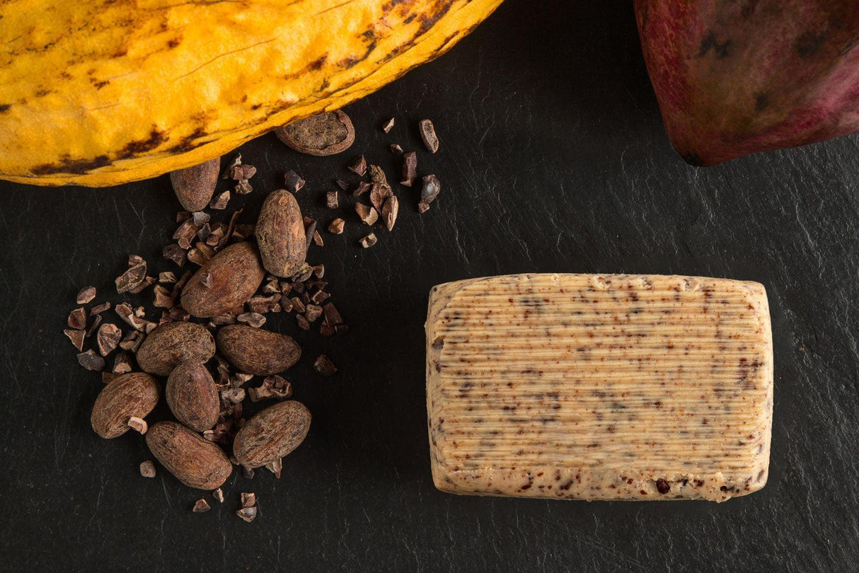 Artisan butter with cocoa nibs, whole cacao beans, and fresh cacao pod on dark slate