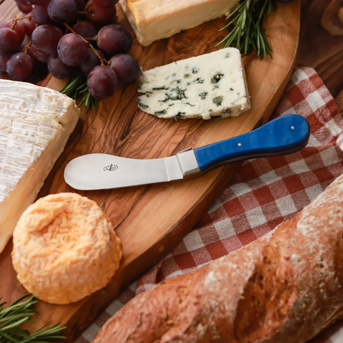 Cheese platter with brie, blue cheese, grapes, baguette, and a blue handled cheese knife.
