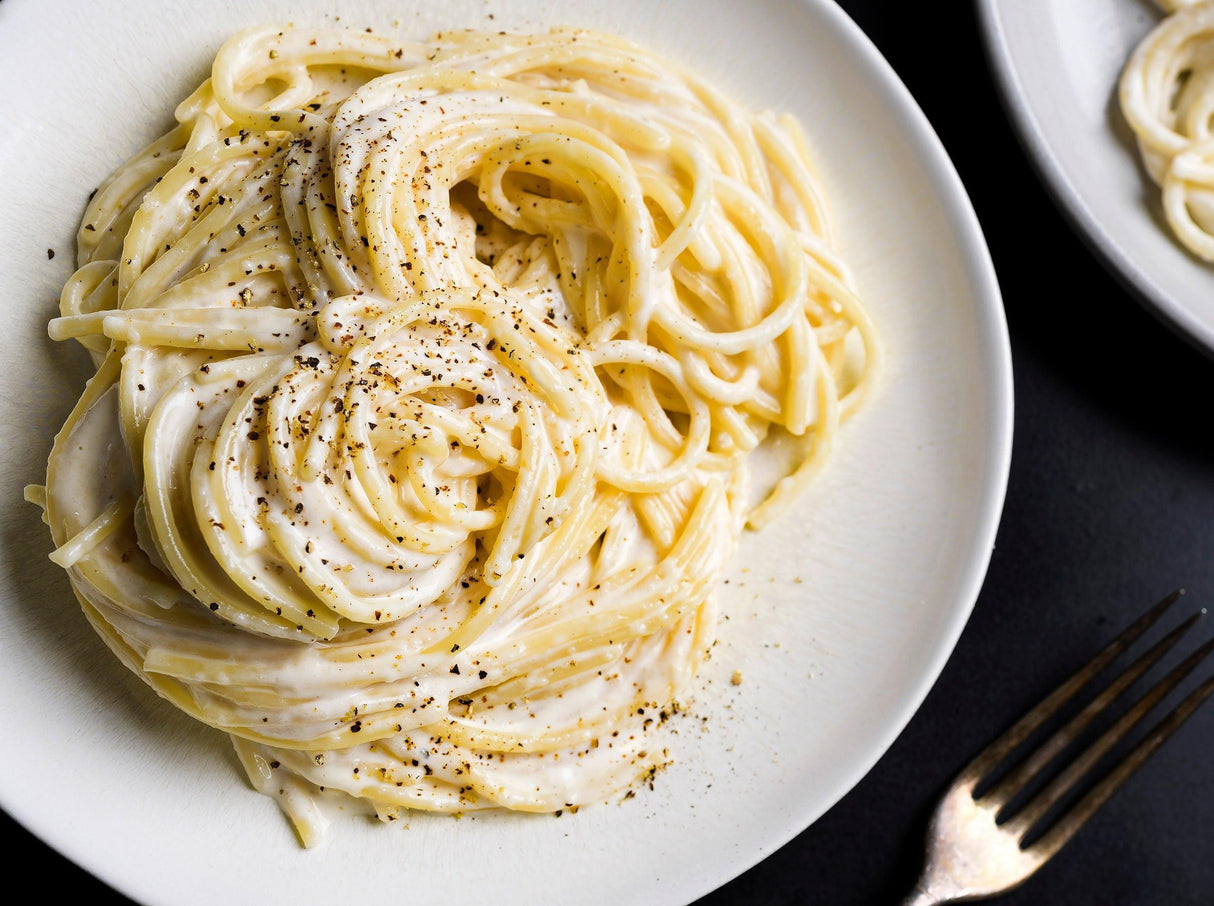 Creamy Parmesan pasta on white plate, topped with cracked black pepper, French Pantry quality