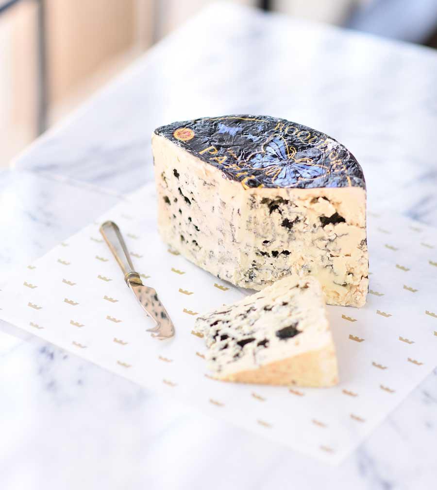 Artisan blue cheese wedge with marbled texture, served on marble with gold-patterned paper and cheese knife