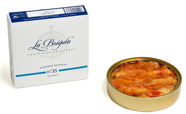 Open tin of Spanish sardines in sauce next to white artisan seafood packaging