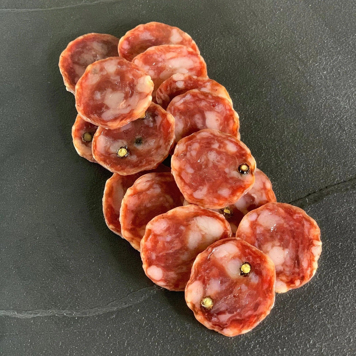 Sliced artisan salami with visible herbs, premium quality, gluten-free, keto-friendly, on dark slate