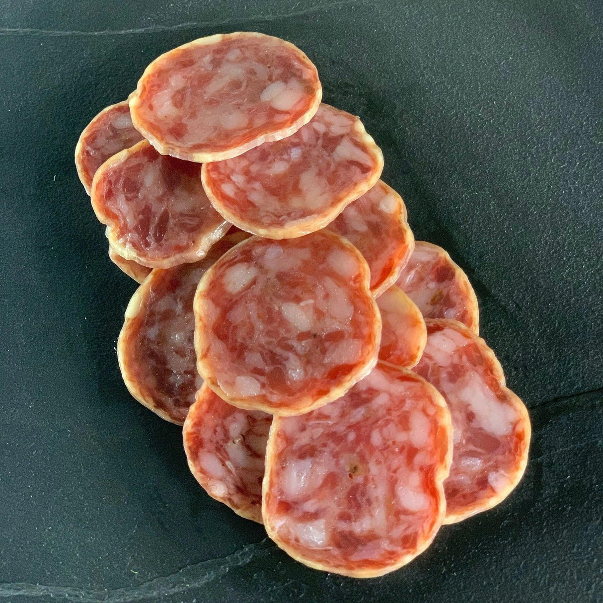 Sliced artisan salami on dark slate, premium quality, gluten-free, keto-friendly, high-protein