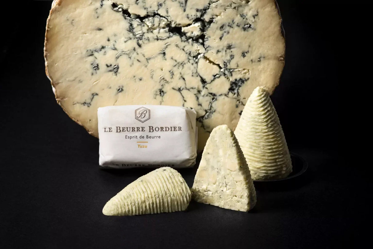 Le Beurre Bordier Yuzu pack with butter quenelles in front of a blue cheese wheel, hand-churned French butter