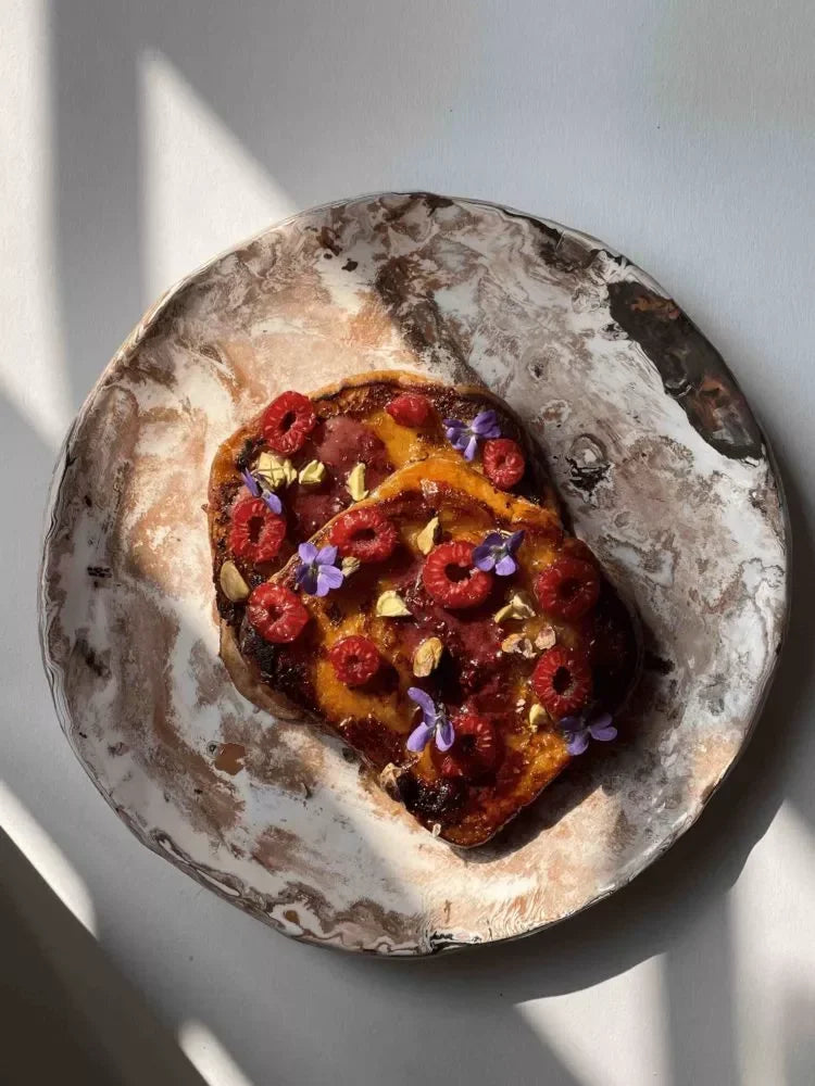 Artisan French toast topped with raspberries, edible flowers, and nuts on a rustic plate