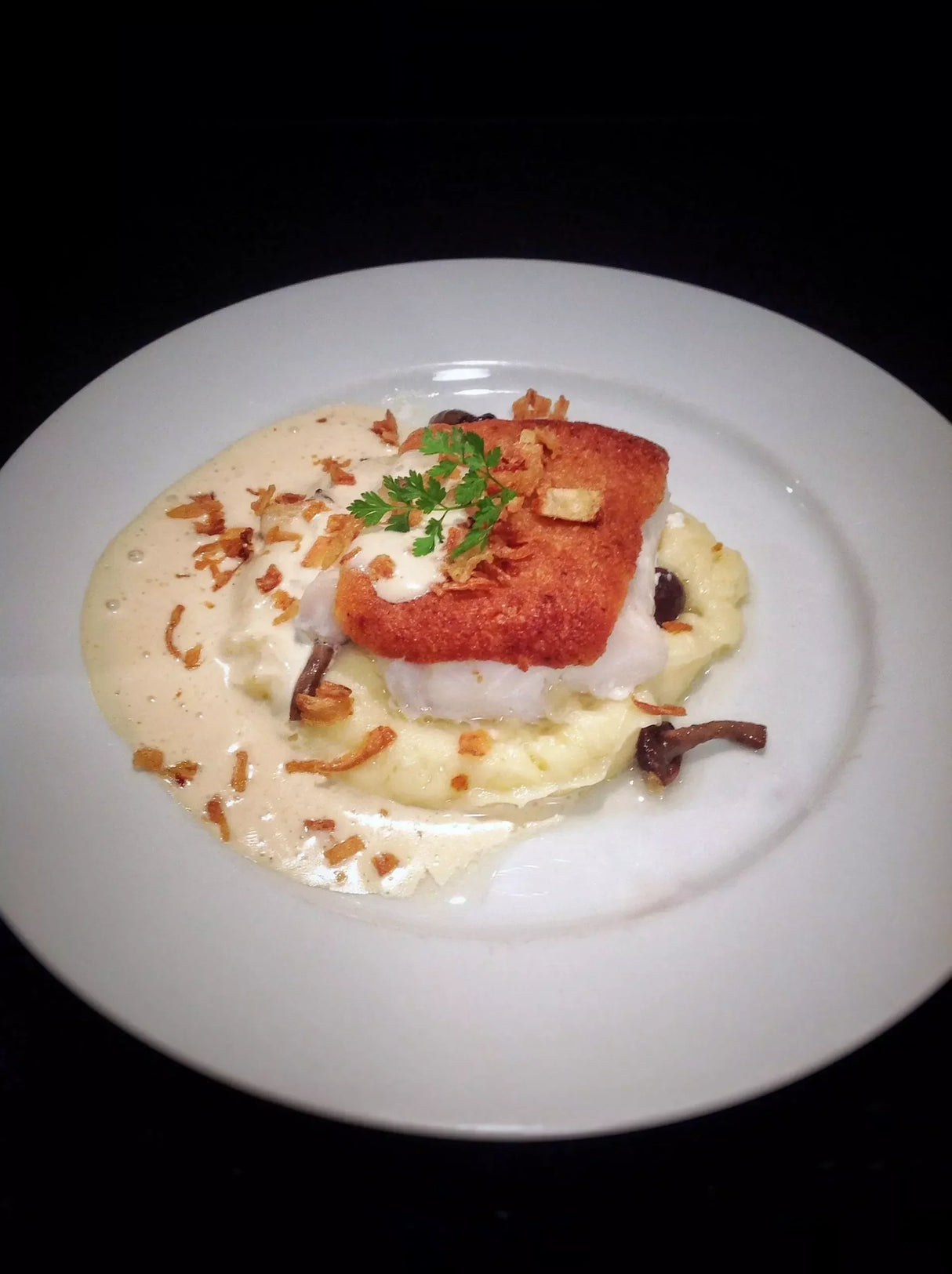 Crispy fish fillet over mashed potatoes with creamy sauce and herbs