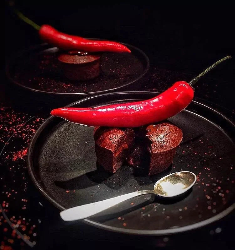Decadent chocolate lava cake with red chili pepper garnish, artisan dessert on black plate