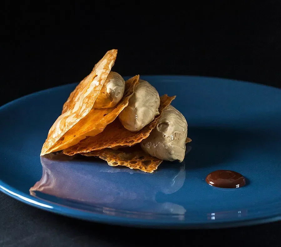 Artisanal French dessert with crispy pastry, creamy mousse, and chocolate drizzle on blue plate