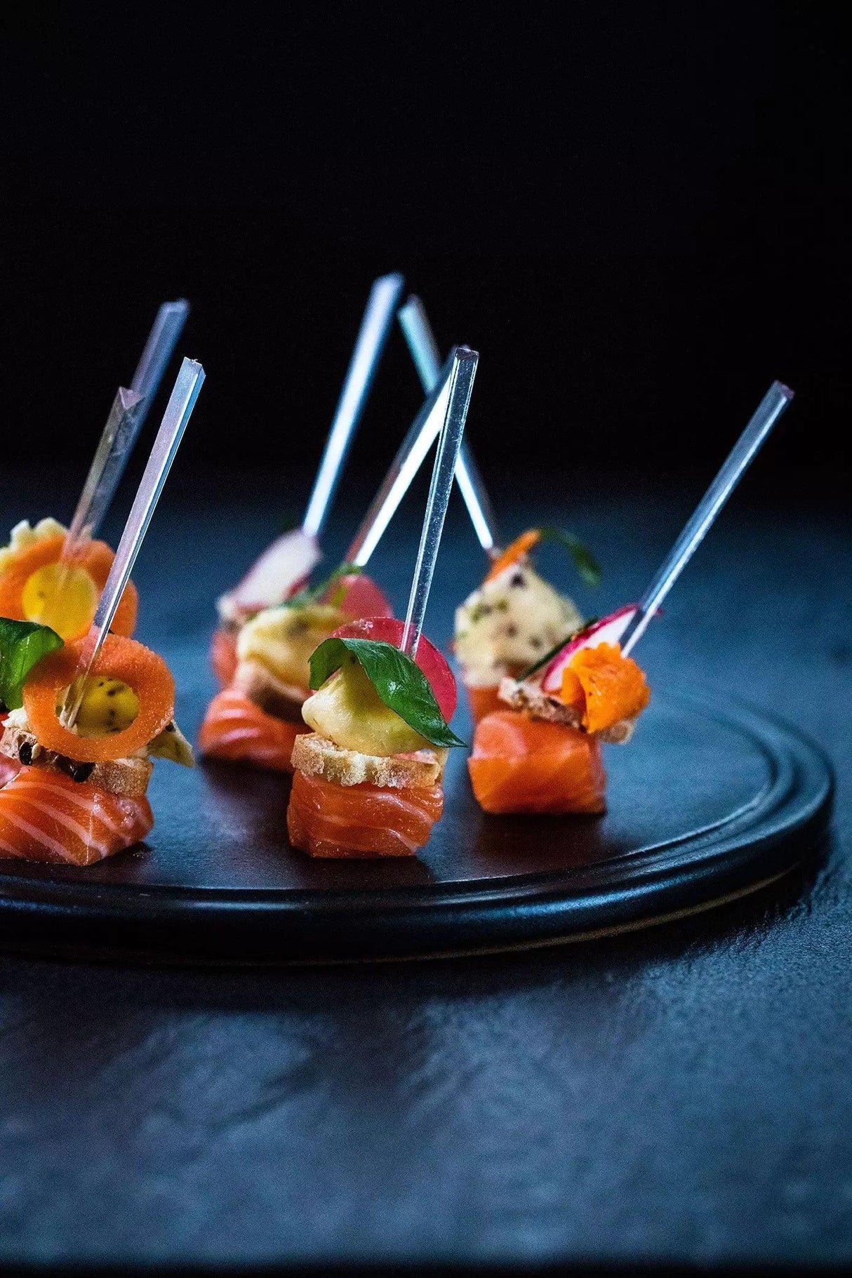 Elegant salmon appetizers with herbs and cream on black plate, artisan-made gourmet bites