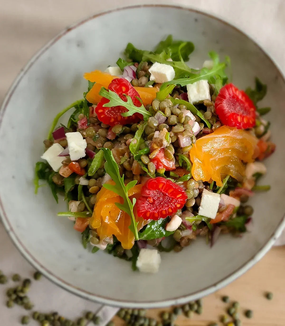 Lentil salad with arugula, smoked salmon, feta, and cherry tomatoes in a rustic bowl