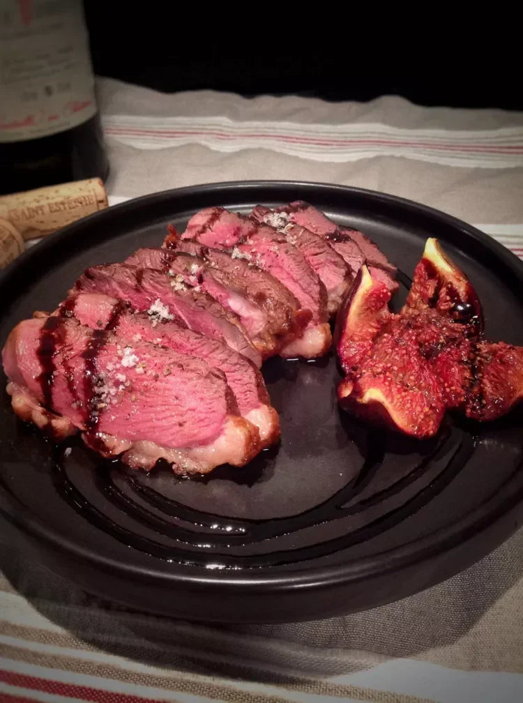 Sliced medium-rare steak with roasted figs, sea salt, and balsamic drizzle on black plate