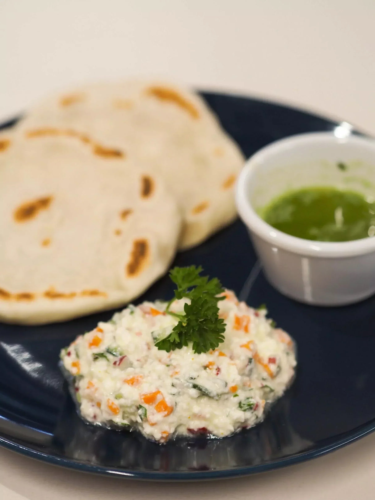 Creamy vegetable dip with naan bread and green sauce on a dark plate