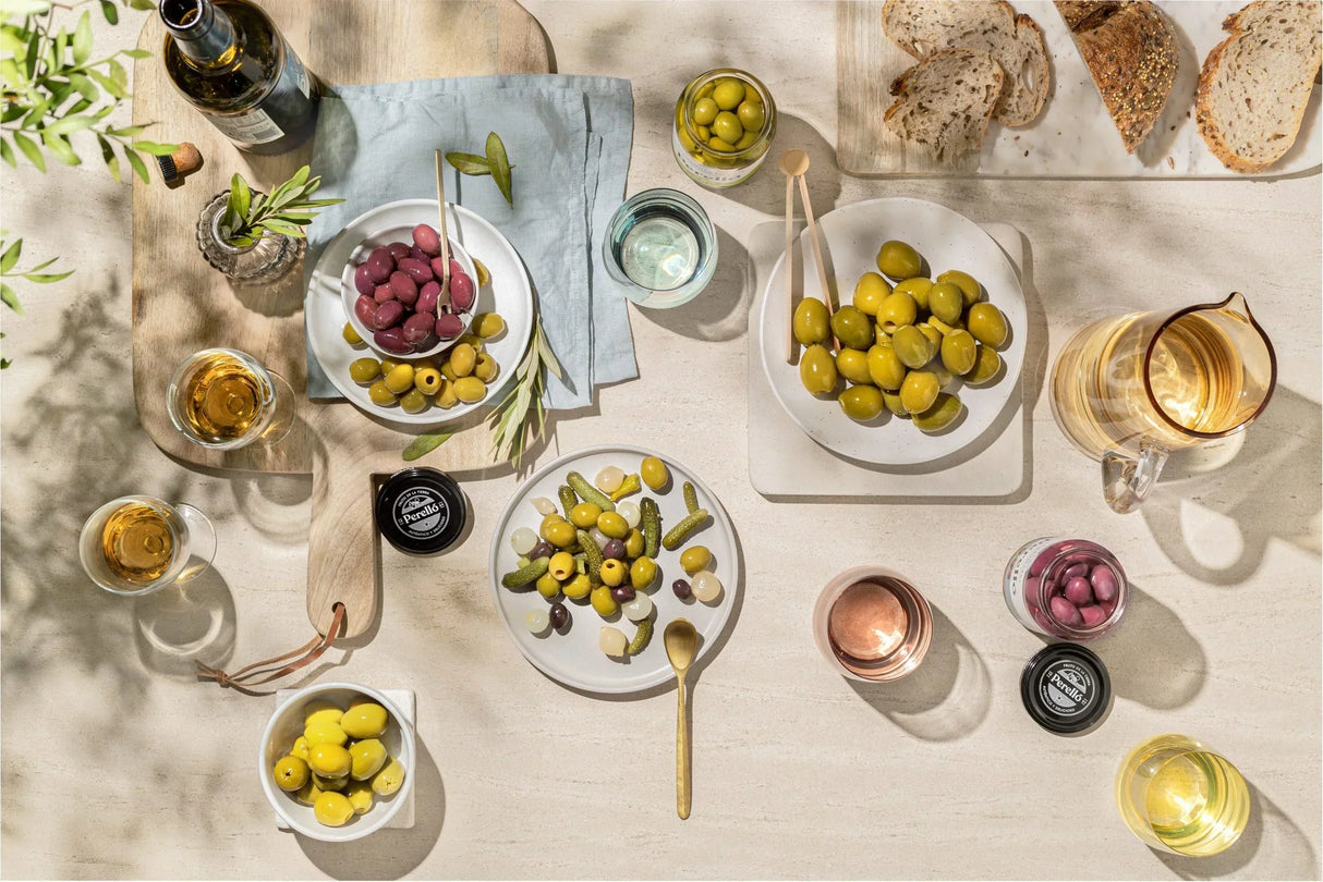 Assorted green and purple olives, pickles, bread, wine and olive oil on a light table