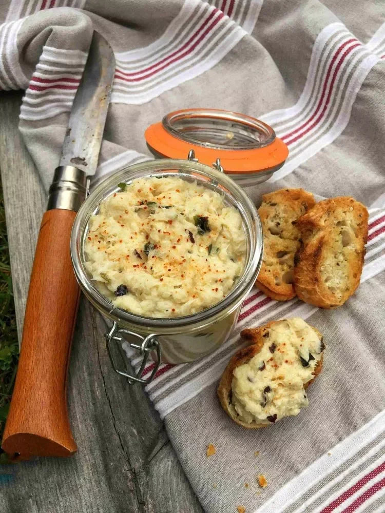 Artisan French spread with herbs, served on toasted bread, alongside a rustic knife on a striped cloth.