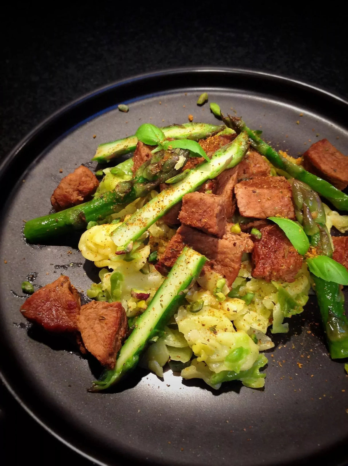 Savory beef cubes with asparagus and cabbage, seasoned with herbs on a dark plate