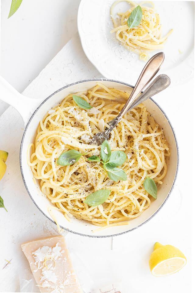 Creamy pasta with fresh basil, lemon, and grated cheese in a white skillet, artisan, premium quality