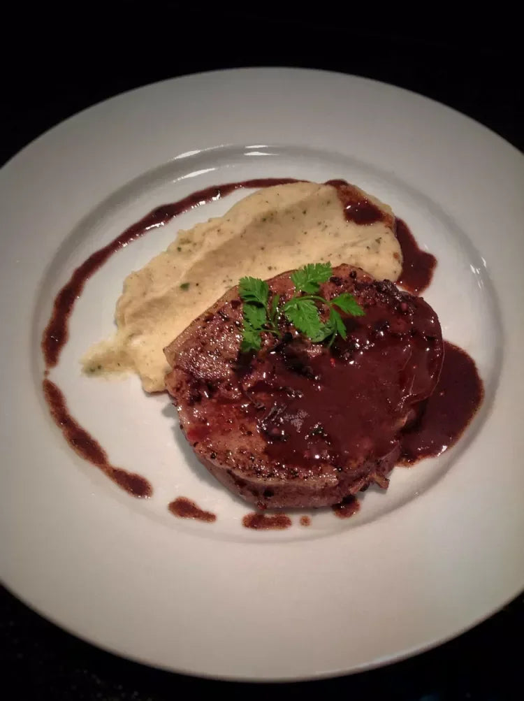 Seared steak with herb butter sauce and mashed potatoes, garnished with parsley