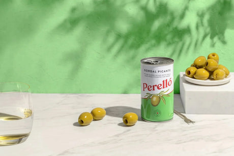 Perelló pitted queen olives with chili, artisanal Spanish olives on marble with white wine, green backdrop