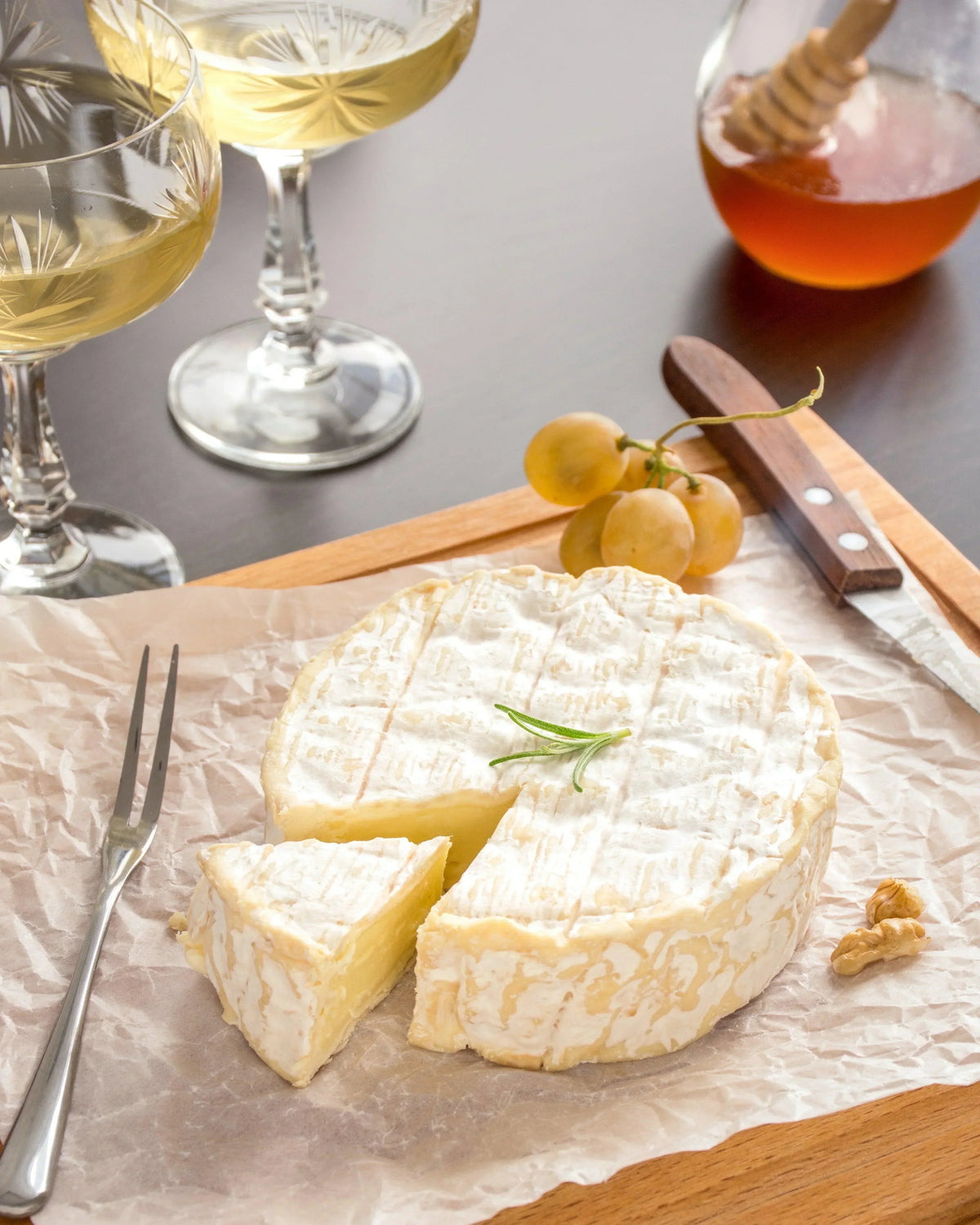French cheese wheel with rosemary, grapes, honey, and white wine for pairing