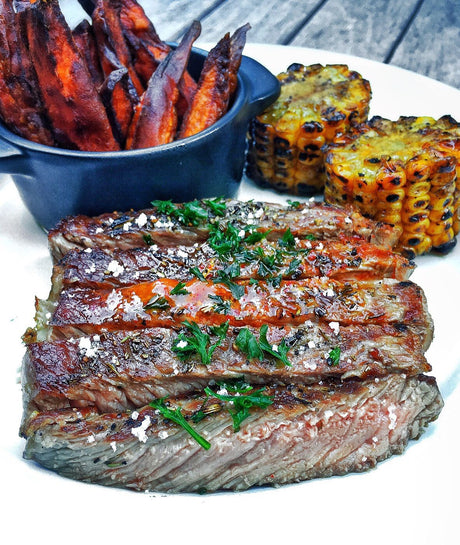 Sliced rib eye steak with sweet potato fries and buttered corn on the cob