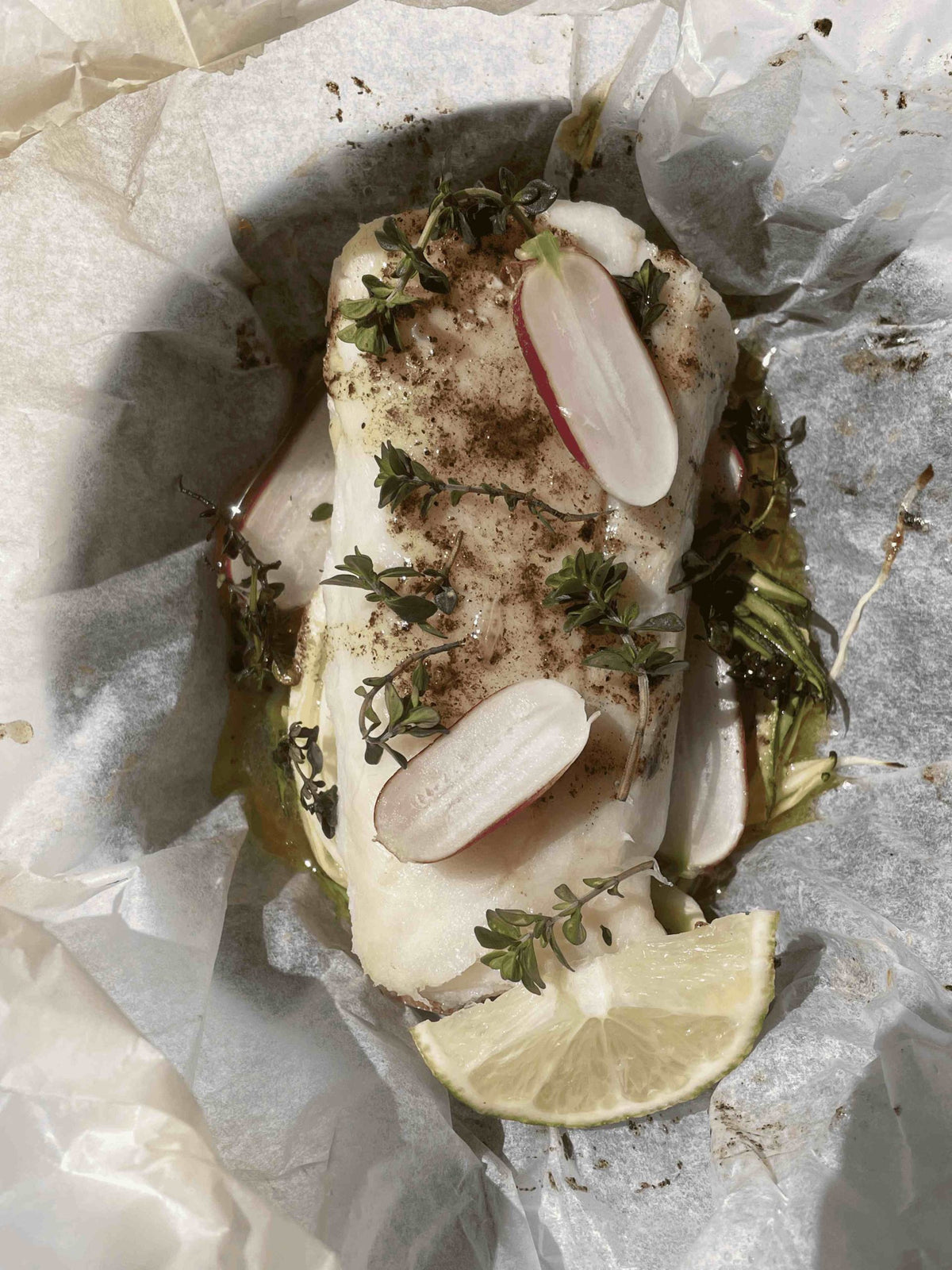 Cod fillet baked in a paper parcel with zucchini ribbons, sliced radishes, thyme and vanilla butter