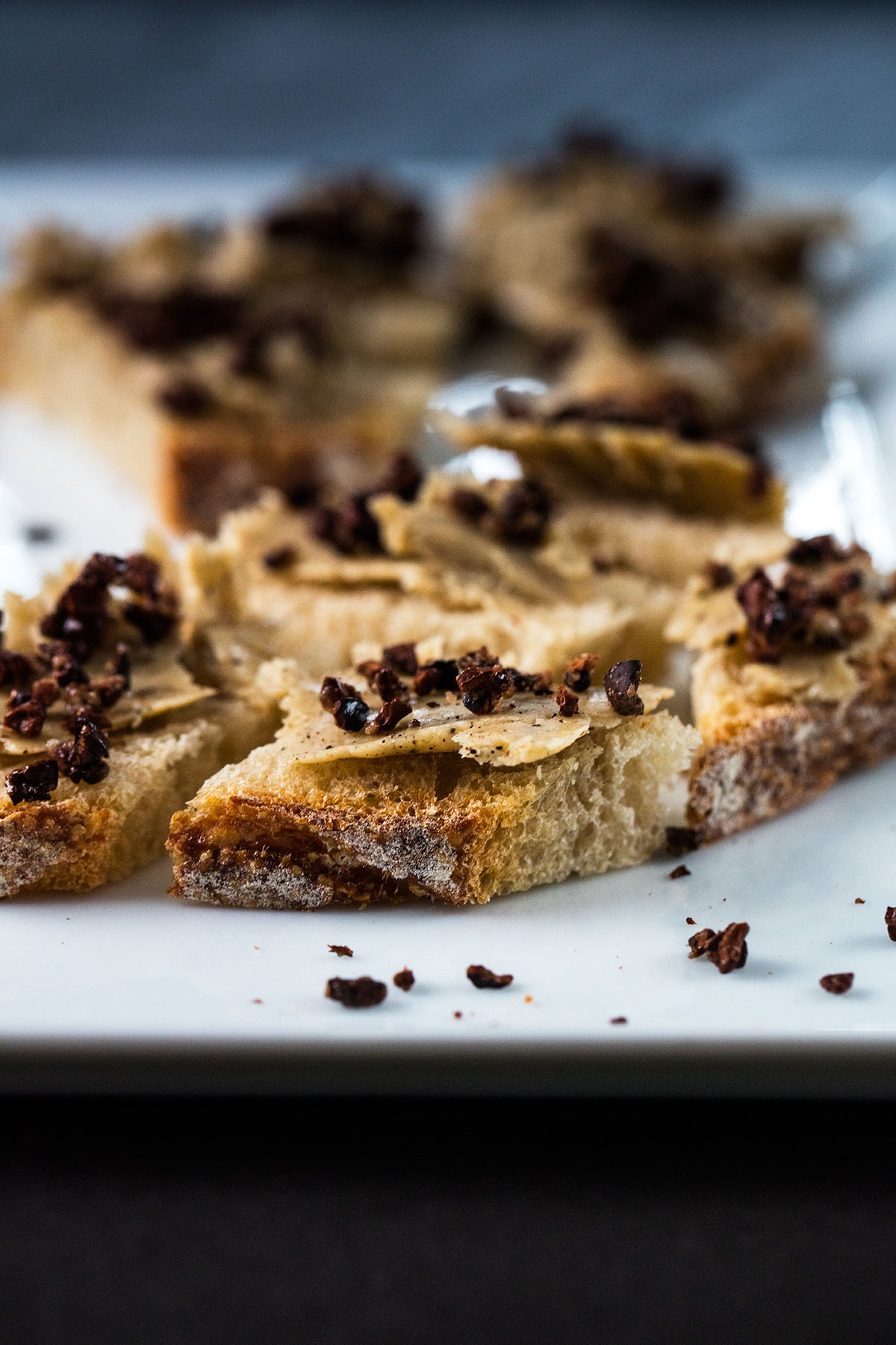 Slices of toasted farmhouse bread topped with shavings of vanilla butter and caramelized cocoa nibs