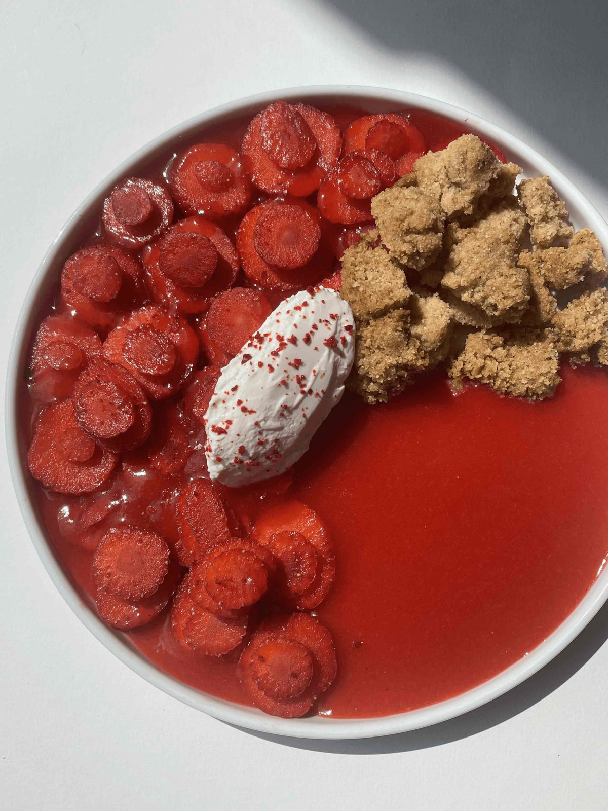 Sliced strawberries plated with almond crumble, strawberry chilli coulis and a spoonful of fresh white cheese